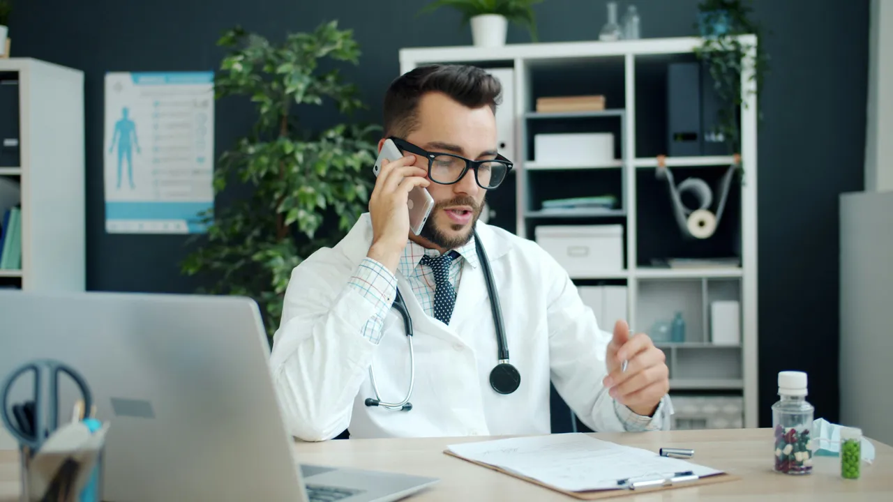 Un médecin dans un cabinet prend un appel à son bureau, le stéthoscope autour du cou.