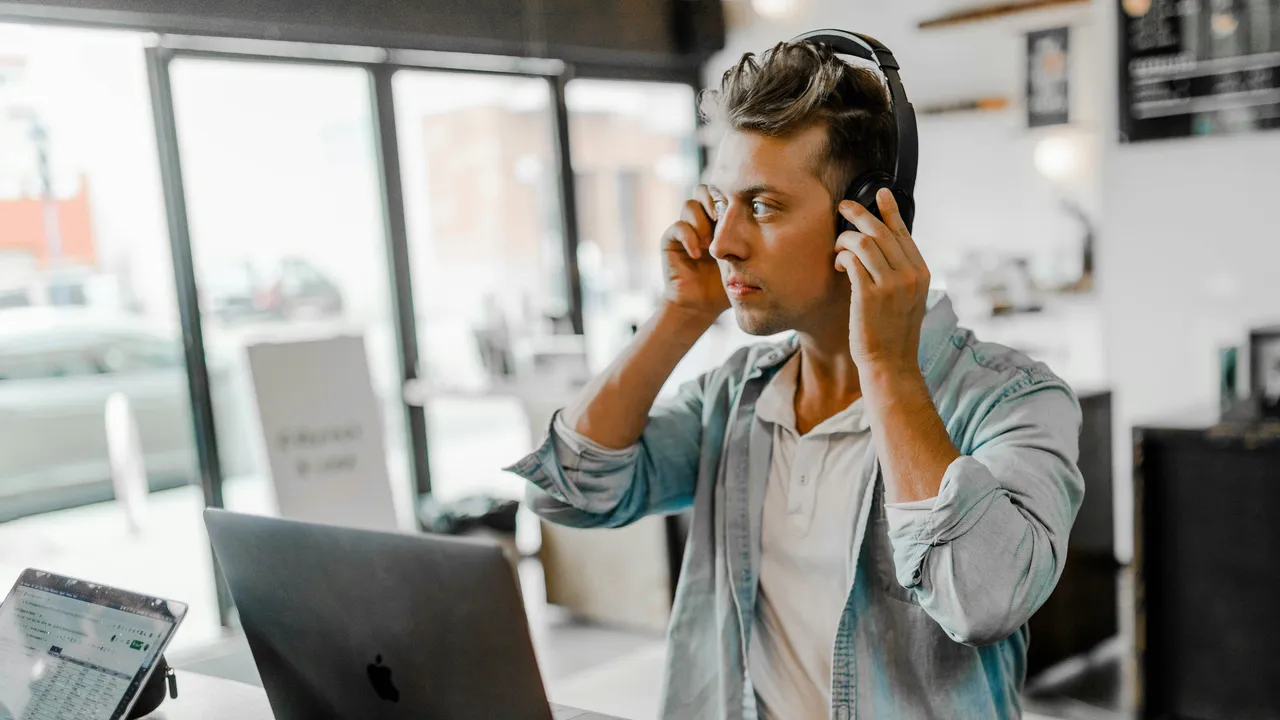 Une personne prend un appel professionnel avec un casque à un bureau à domicile, devant un ordinateur portable.
