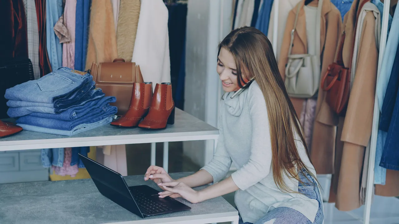Une commerçante au téléphone derrière le comptoir d'une boutique de prêt-à-porter.